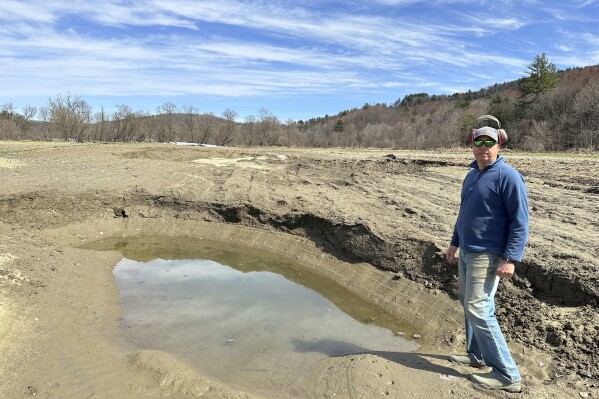 Farmer George Gross, of Dog River Farm in Berlin, Vt., stands, Wednesday, April 17, 2024, next to a hole left in his field by December, 2023, flooding. The farm lost nearly all of its produce in the catastrophic summer flooding that hit Vermont in July. (AP Photo/Lisa Rathke)