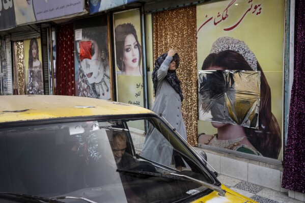 FILE - A woman walks past a beauty salon with window decorations which have been defaced in Kabul, Afghanistan, Sunday, Sept. 12, 2021. The one-month dateline given to women beauty salons ban in Afghanistan ended Tuesday, July 25, 2023. Taliban say that beauty salons must stop their activities otherwise their licenses will be cancelled. Sadiq Akif Mahjer, the spokesman for the Taliban-run Virtue and Vice Ministry says Tuesday that if they do not obey the orders of the ministry, their licenses will be cancelled by the municipality. (AP Photo/Bernat Armangue, File)
