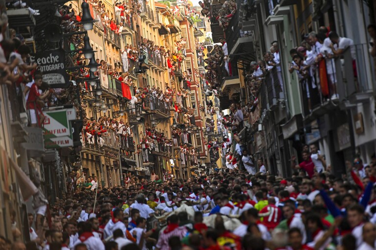 Revellers, mostly tourists, look on from balconies at the running of the bulls during the San Fermín fiestas in Pamplona, Spain, Saturday, July 8, 2023. Crowds are packing the Colosseum, the Louvre, the Acropolis and other major attractions as tourism exceeds 2019 records in some of Europe’s most popular destinations. While European tourists helped the industry on the road to recovery last year, the upswing this summer is led largely by Americans, who are lifted by a strong dollar and in some cases pandemic savings. (AP Photo/Alvaro Barrientos)