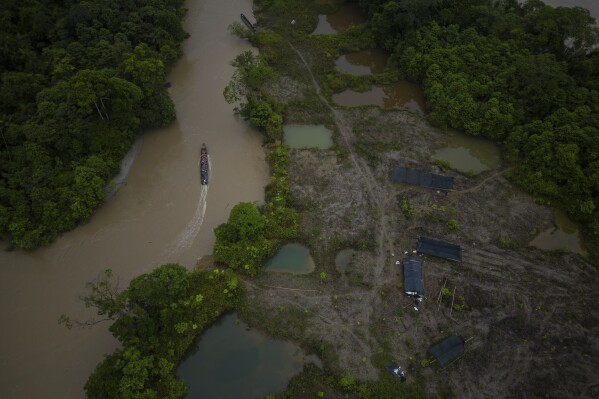 A boat, with gasoline to be taken to illegal mining machinery, maneuvers past an area that was mined near Paimado, Colombia, Sept. 24, 2024. (AP Photo/Ivan Valencia, File)