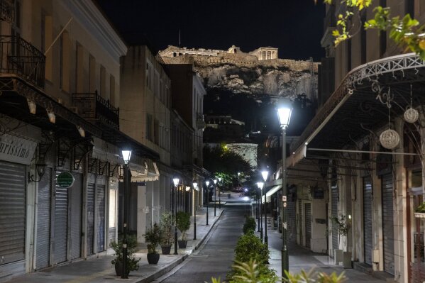 This photo shows a view of an empty street with the hill of the Acropolis at the background in Athens, Greece, Sunday, Oct. 25, 2020. Greece's government has imposed a nightly curfew in greater Athens and other areas with high infection rates as well as a mask requirement. (AP Photo/Yorgos Karahalis)