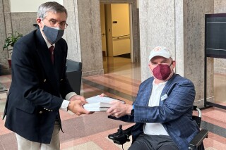 In this photo provided by I AM ALS, Dan Tate, right, delivers a printed petition from ALS patients and advocates to Dr. Peter Marks, left, director of the Food and Drug Administration's center for biologics at the FDA campus in Silver Spring, Md., on Dec. 14, 2022. The FDA meets this week to consider approval of an experimental treatment for Lou Gehrig’s disease, the culmination of a yearslong lobbying effort by patients with the fatal, neurodegenerative disease. Those advocates still face one giant hurdle: FDA regulators say the treatment hasn't been shown to work. In documents posted Monday, Sept. 25, 2023 the FDA reiterated its longstanding position: drugmaker Brainstorm's lone study doesn't provide clear evidence that its stem cell-based therapy helps patients with ALS, or amyotrophic lateral sclerosis. (Sonya Elling/I AM ALS via AP)