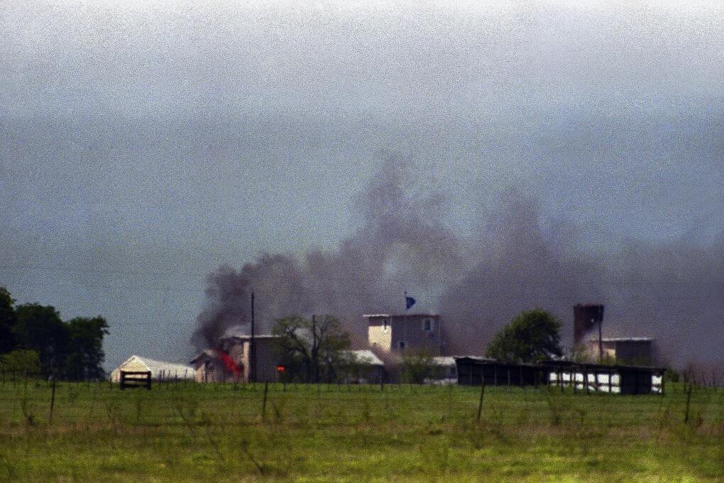 Flames are seen in building to right of tower and smoke billows into sky as the fire first becomes visible at the Branch Davidian compound near Waco, Texas on Monday, April 19, 1993. The compound burned to the ground and the Justice Department said cult members set the fire. (AP Photo/Roberto Borea)