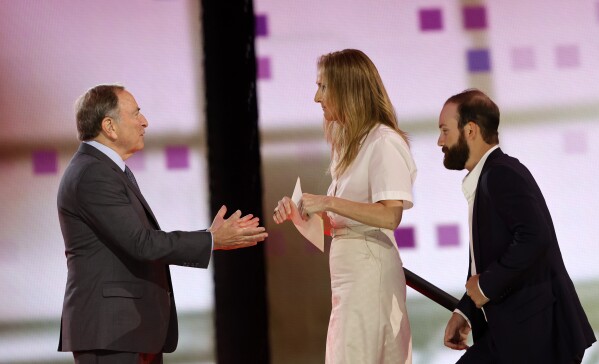 NHL Commissioner Gary Bettman, left, welcomes singer Celine Dion onto the stage during the first round of the NHL hockey draft Friday, June 28, 2024, in Las Vegas. Dion helped announce the selection of Ivan Demidov by the Montreal Canadiens. (AP Photo/Steve Marcus)