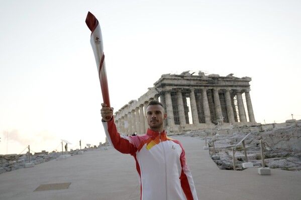 FILE - Greek torch bearer Christos Volikakis, world Champion in Cycling, holds the Olympic torch in front of ancient Parthenon temple atop of the Acropolis hill in Athens, Oct. 19, 2021. Four-time Olympic cyclist Christos Volikákis tested positive for doping in retests of samples from the 2016 Rio de Janeiro Games, the International Cycling Union said Friday, March 15, 2024. (AP Photo/Petros Giannakouris, File)