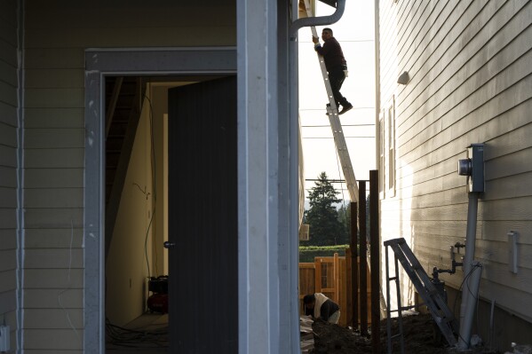 With the so-called urban growth boundary in the background, a worker climbs down a ladder while working on a new construction home on Thursday, Feb. 22, 2024, in the southwest Portland, Ore., suburb of Tigard. The boundary was established by a 1973 law that placed boundaries around cities to prevent urban sprawl and preserve nature and farmland. (AP Photo/Jenny Kane)