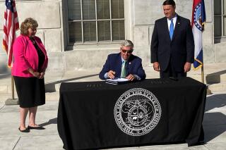 Missouri Gov. Mike Parson signs legislation limiting the during of local public health orders during a ceremony Tuesday, June 15, 2021, outside the state Capitol in Jefferson City, Mo. The new law took effect immediately and was passed in response to local restrictions imposed during the coronavirus pandemic. Among its supporters were state Sen. Sandy Crawford, left, and House Speaker Pro Tem John Wiemann. (AP Photo/David A. Lieb)