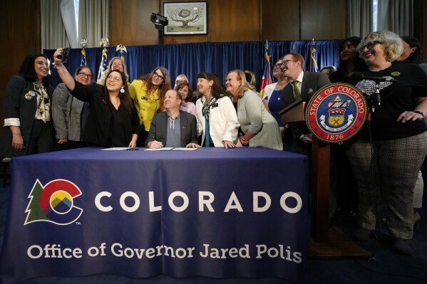 FILE - Colorado State Sen. Julie Gonzales, third from left, takes a photo of state Rep. Brianna Titone, Colorado Gov. Jared Polis, state Sen. Sonya Jaquez Lewis and state Rep. Meg Froelich and others before Polis signed the first of three bills that enshrine protections for abortion and gender-affirming care procedures and medications, April 14, 2023, in the State Capitol in Denver. Voters in both Colorado and South Dakota will have a say on abortion rights this fall after supporters collected enough valid signatures to put measures on the ballot. (AP Photo/David Zalubowski,File)