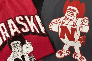 Nebraska Huskers t-shirts featuring new cartoon mascot Herbie Husker, left, and old cartoon mascot, right, are displayed at the Husker Hounds store in Omaha, Neb., Saturday, Jan. 29, 2022. The University of Nebraska-Lincoln has made a change to its cartoon mascot Herbie Husker to eliminate confusion about the meaning of a hand gesture he makes that some people connect with white supremacy.(AP Photo/Eric Olson)