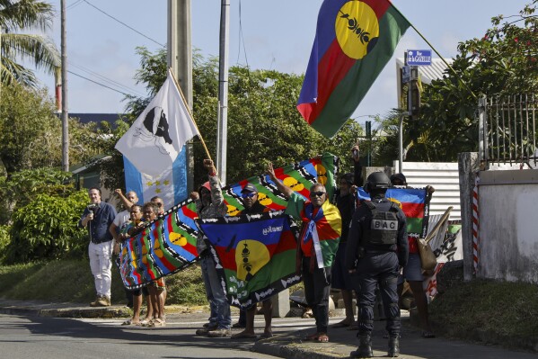 People demonstrate as French President Emmanuel Macron's motorcade drives past in in Noumea, New Caledonia, Thursday, May 23, 2024. Macron has landed in riot-hit New Caledonia, having crossed the globe by plane from Paris in a high-profile show of support for the French Pacific archipelago wracked by deadly unrest and where indigenous people have long sought independence from France. (Ludovic Marin/Pool Photo via AP)