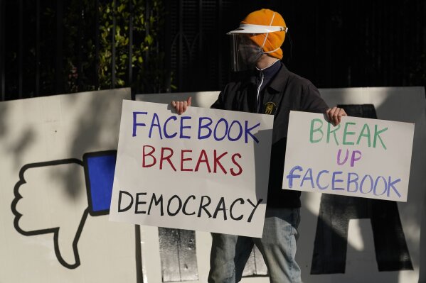FILE - In this Saturday, Nov. 21, 2020, file photo, a demonstrator joins others outside of the home of Facebook CEO Mark Zuckerberg to protest what they say is Facebook spreading disinformation in San Francisco. Federal regulators asked Wednesday, Dec. 9, 2020, for Facebook to be ordered to divest its Instagram and WhatsApp messaging services as the U.S. government and 48 states and districts accused the company of abusing its market power in social networking to crush smaller competitors. The antitrust lawsuits were announced by the Federal Trade Commission and New York Attorney General Letitia James. (AP Photo/Jeff Chiu, File)