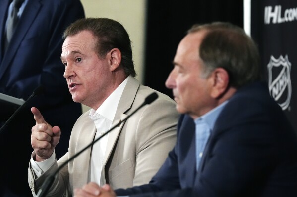 Arizona Coyotes Chairman and Governor Alex Meruelo, left, speaks as NHL Commissioner Gary Bettman, right, listens as they hold a news conference regarding a provision for Arizona to get an expansion team if a new arena is built within the next five years with the announcement of the current team relocating to Salt Lake City, Friday, April 19, 2024, in Phoenix. The Coyotes are officially headed to Salt Lake City after NHL Board of Governors voted Thursday to approve a $1.2 billion sale from Meruelo to Utah Jazz owner Ryan Smith, with Meruelo retaining the Coyotes' name, logo and trademark. (AP Photo/Ross D. Franklin)