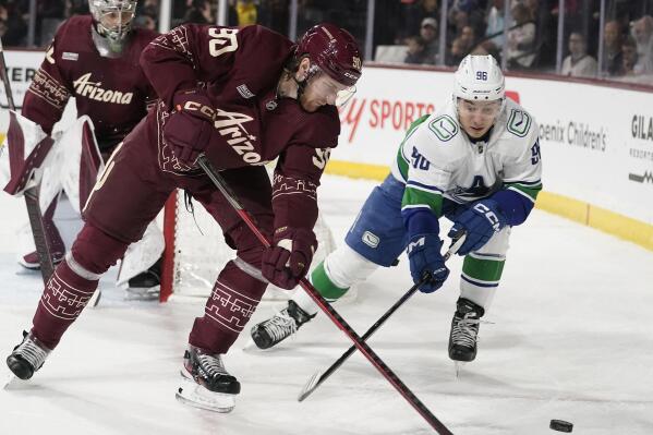 Vancouver Canucks' Andrei Kuzmenko (96) chases the puck against Arizona Coyotes' J.J. Moser (90) during the first period of an NHL hockey game Thursday, March 16, 2023, in Tempe, Ariz. (AP Photo/Darryl Webb)