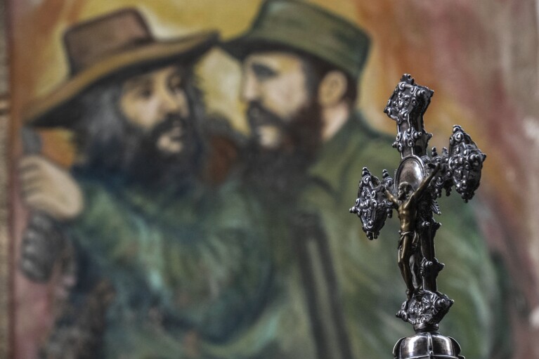 FILE - A crucifix is carried by faithful during a Holy Week procession backdropped by a mural of Fidel Castro and Camilo Cienfuegos, in Havana, Cuba, March 29, 2024. The 1959 revolution led by Castro installed an atheist, Communist government that sought to replace the Catholic Church as the guiding force in the lives of Cubans. (AP Photo/Ramon Espinosa, File)