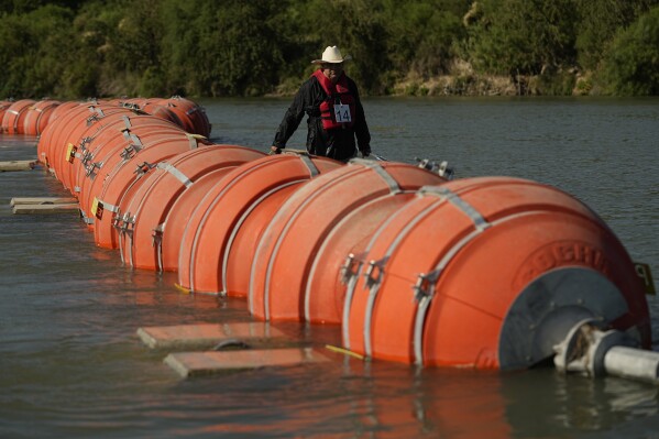 FILE - A kayaker walks past large buoys being used as a floating border barrier on the Rio Grande, Aug. 1, 2023, in Eagle Pass, Texas. The 5th U.S. Circuit Court of Appeals heard arguments on the future of the barrier of giant buoys that aimed at deterring migrant traffic on Wednesday, May 15, 2024. (AP Photo/Eric Gay, File)