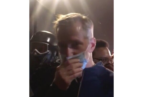 In this image made from video released by Karina Brown, Portland Mayor Ted Wheeler puts his hands to his mouth as he stands at a fence guarding a federal courthouse as tear gas drifts by early July 23, 2020, in Portland Oregon, during another night of protest against the presence of federal agents sent by President Donald Trump to quell unrest in the city. (Karina Brown via AP)