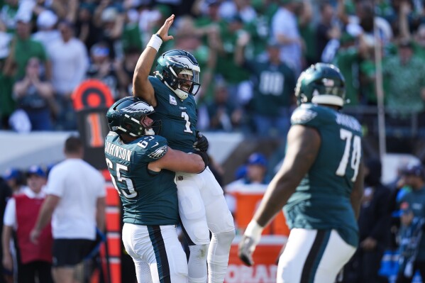 Philadelphia Eagles quarterback Jalen Hurts (1) is lifted by Eagles offensive tackle Lane Johnson (65) after Hurts threw a touchdown pass to Eagles wide receiver DeVonta Smith during the second half of an NFL football game against the Cleveland Browns on Sunday, Oct. 13, 2024, in Philadelphia. (AP Photo/Chris Szagola)