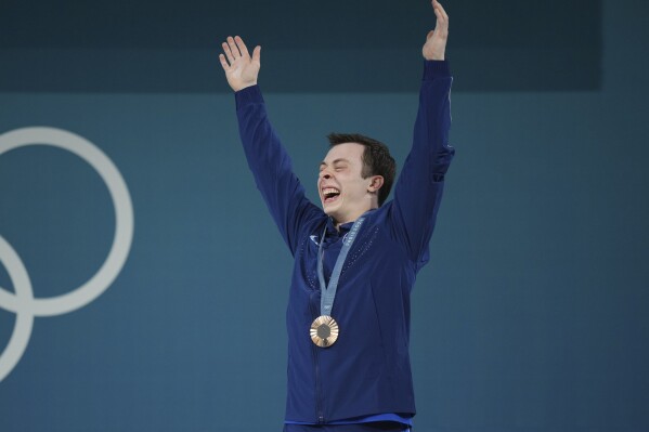 Bronze medalist Hampton Morris of the United States celebrates on the podium during the medal ceremony for the men's 61kg weightlifting event at the 2024 Summer Olympics, Wednesday, Aug. 7, 2024, in Paris, France. (AP Photo/Kin Cheung)