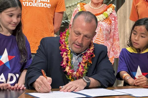 Hawaii Gov. Josh Green signs gun control legislation in Honolulu on Friday, June 2, 2023 as Leia Kandell, left, age 10, and Cole Kandell, age 7, look on. Green signed legislation that allows more people to carry concealed firearms but at the same time prohibit people from taking guns to a wide range of places, including beaches, hospitals, stadiums, bars that serve alcohol and movie theaters. (AP Photo/Audrey McAvoy)