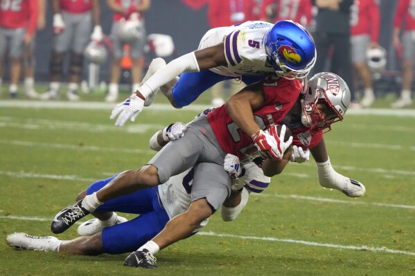 UNLV wide receiver Jacob De Jesus is tackled by Kansas safety O.J. Burroughs (5) and linebacker Taiwan Berryhill Jr. during the first half of the Guaranteed Rate Bowl NCAA college football game Tuesday, Dec. 26, 2023, in Phoenix. (AP Photo/Rick Scuteri)