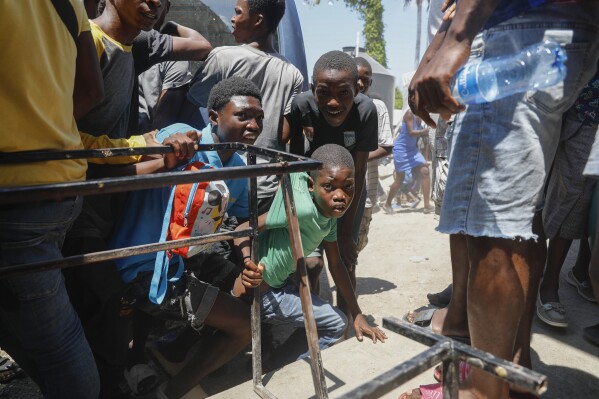 Unos jóvenes se agachan tras escuchar disparos en una escuela que sirve de albergue para personas desplazadas por la violencia de las pandillas, en Puerto Príncipe, Haití, el 22 de marzo de 2024. (Foto AP/Odelyn Joseph)