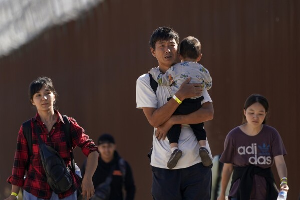 A group of people, including many from China, walk along the wall after crossing the border with Mexico to seek asylum, Tuesday, Oct. 24, 2023, near Jacumba, Calif. A major influx of Chinese migration to the United States on a relatively new and perilous route through Panama's Darién Gap jungle has become increasingly popular thanks to social media. (AP Photo/Gregory Bull)