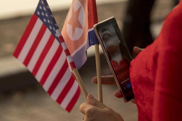 FILE - In this Feb. 27, 2019, file photo a woman holds American and North Korean flags as she walks along Sword Lake in Hanoi, Vietnam. The Biden administration has extended for one year a Trump-era ban on the use of U.S. passports for travel to North Korea.  The ban had first been imposed by former Secretary of State Rex Tillerson in 2017 after the death of American student Otto Warmbier who suffered grievous injuries while in North Korean custody. It has been extended annually ever since. (AP Photo/Andrew Harnik, File)