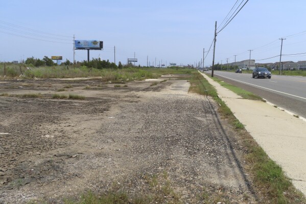 A car drives past a vacant lot, Wednesday, July 27, 2023, in Egg Harbor Township, N.J., where a string of seedy motels used to stand. In November 2006, the bodies of four Atlantic City-area sex workers were found in a drainage ditch behind the motels, four of many such cases that remain unsolved around the U.S. (AP Photo/Wayne Parry)