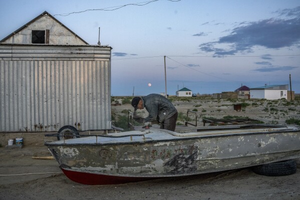 A man repairs an old boat along the dried-up Aral Sea, in the village of Tastubek near the Aralsk city, Kazakhstan, Monday, July 2, 2023. (AP Photo/Ebrahim Noroozi)