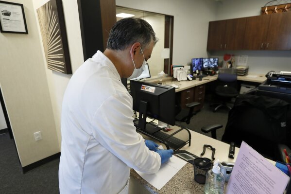 Dermatologist Dr. Seemal Desai works in his office in Plano, Texas, Thursday, May 7, 2020. Desai said patient visits for his Dallas-area dermatology practice plunged about 85% after COVID-19 hit. (AP Photo/Tony Gutierrez)