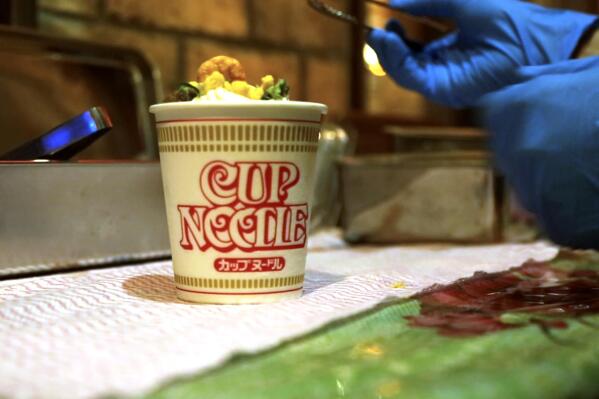 A Cup Noodle ice cream, made with the powdered soup of Cup Noodle and topped with freeze-fried shrimp, onions, egg and meat, is prepared to be eaten at the Cup Noodles Museum in Yokohama, Japan, on Friday, Aug. 6, 2021. Sold only at the Yokohama museum, the ice cream embodies a spirit of adventure in Japanese foods. (AP Photo/John Leicester)