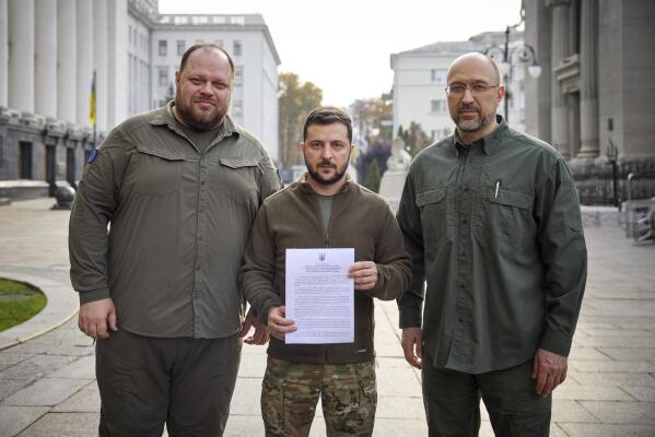 In this photo provided by the Ukrainian Presidential Press Office, Ukrainian President Volodymyr Zelenskyy, center, alongside Prime Minister Denys Shmyhal, right, and the head of Verkhovna Rada (Supreme Council of Ukraine) Ruslan Stefanchuk, holds an application for ''accelerated accession to NATO'' in Kyiv, Ukraine, Friday Sept. 30, 2022. (Ukrainian Presidential Press Office via AP)