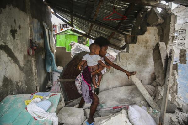 A woman carries her child as she walks in the remains of her home destroyed by Saturday´s  7.2 magnitude earthquake in Les Cayes, Haiti, Sunday, Aug. 15, 2021. (AP Photo/Joseph Odelyn)