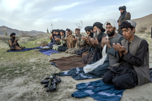 Taliban fighters and other men pray in a cemetery in a village in a remote region of Afghanistan, on Friday, Feb. 24, 2023. A farmer, his wife and their five children killed during a Sept. 5, 2019, night raid by U.S. forces, were buried here, where generations of their kin had been laid to rest. (AP Photo/Ebrahim Noroozi)