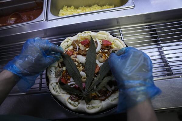 A cannabis leaf is put on a pizza at a restaurant in Bangkok, Thailand on Nov. 24, 2021. The Pizza Company, a Thai major fast food chain, has been promoting its "Crazy Happy Pizza" this month, an under-the-radar product topped with a cannabis leaf. It’s legal but won’t get you high.  (AP Photo/Sakchai Lalit)