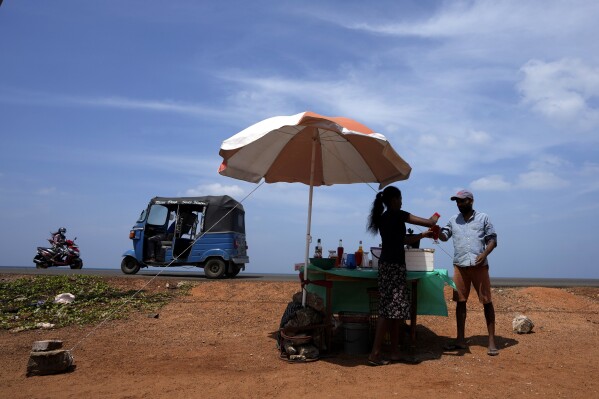 FILE - A man buys a cool drink from a roadside vendor on a sunny day in Mahawewa, a village north of Colombo, Sri Lanka, Feb. 29, 2024. A new study says climate change will reduce future global income by about 19% in the next 25 years compared to a fictional world that’s not warming. (AP Photo/Eranga Jayawardena, File)