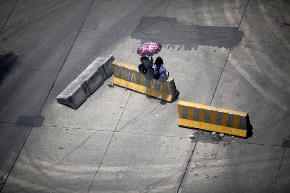 Women sit on at traffic barrier, one of many used by supporters of former President Evo Morales to block a highway in El Alto, Bolivia, Saturday, Nov. 16, 2019. Morales stepped down following nationwide protests over suspected vote-rigging in an Oct. 20 election in which he claimed to have won a fourth term in office. An Organization of American States audit of the vote found widespread irregularities. Morales has denied there was fraud. (AP Photo/Natacha Pisarenko)