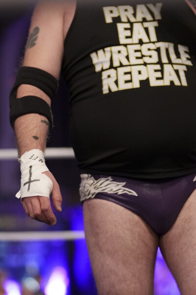 Se ve una cruz en la mano de Gareth "Angel" Thompson, fundador de la organización benéfica Kingdom Wrestling, durante un combate de lucha libre en la iglesia de San Pedro en Shipley, el sábado 29 de marzo de 2025. (Foto AP/Jon Super)