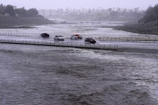 Vehicles cross over a flood control basin that has almost reached the street as Tropical Storm Hilary hits the area, Sunday, Aug. 20, 2023, in Palm Desert, Calif. (AP Photo/Mark J. Terrill)