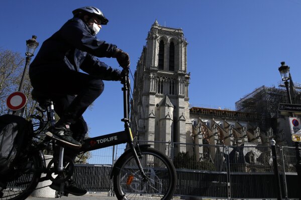 A man wearing a face mask rides his bike in front of Notre Dame cathedral during a nationwide confinement to counter the Covid-19, in Paris, Sunday, April 5, 2020. The new coronavirus causes mild or moderate symptoms for most people, but for some, especially older adults and people with existing health problems, it can cause more severe illness or death. (AP Photo/Christophe Ena)