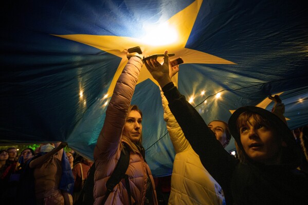 Demonstrators shine the lights of their mobile phones as they stand under a large European Union flag, during a pro-EU rally ahead of the second round of the presidential election redo in Bucharest, Romania, Friday, May 9, 2025. (AP Photo/Andreea Alexandru)