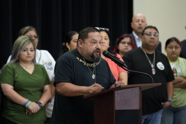 Javier Cazares, center, stands with families of the victims in the Uvalde elementary school shooting during a news conference, Wednesday, May 22, 2024, in Uvalde, Texas. The families of 19 of the victims announced a lawsuit against nearly 100 state police officers who were part of the botched law enforcement response. The families say they also agreed a $2 million settlement with the city, under which city leaders promised higher standards and better training for local police. (AP Photo/Eric Gay)
