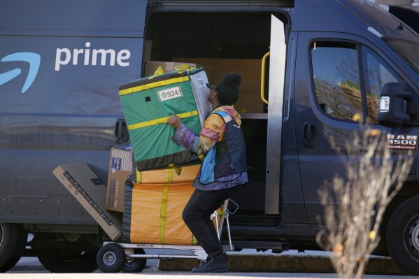 An Amazon Prime delivery person lifts packages while making a stop at an apartment building on Tuesday, Nov. 28, 2023, in Denver. Walmart, Target and Amazon are all-in on the shipping wars, a move retail experts say will help them maintain a competitive edge against low-cost Chinese retailers Shein and Temu. (AP Photo/David Zalubowski)