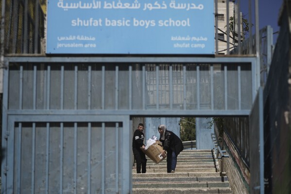 A student and a teacher carry study material at UNRWA Girls School run by the U.N. agency for Palestinian refugees in the Shuafat Refugee Camp in east Jerusalem, Thursday, May 8, 2025. After Israeli forces ordered the closure of six of its schools in east Jerusalem Thursday. (AP Photo/Mahmoud Illean)
