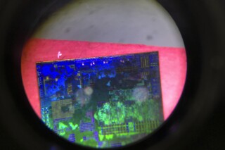 FILE - A Chinese microchip is seen through a microscope set up at the booth for the state-controlled Tsinghua Unigroup project which is aimed at driving China's semiconductor ambitions during the 21st China Beijing International High-tech Expo in Beijing, China, on May 17, 2018. China has imposed export curbs on two metals used in computer chips and solar cells, expanding a squabble with Washington over high-tech trade ahead of Treasury Secretary Janet Yellen's visit to Beijing this week. (AP Photo/Ng Han Guan, File)