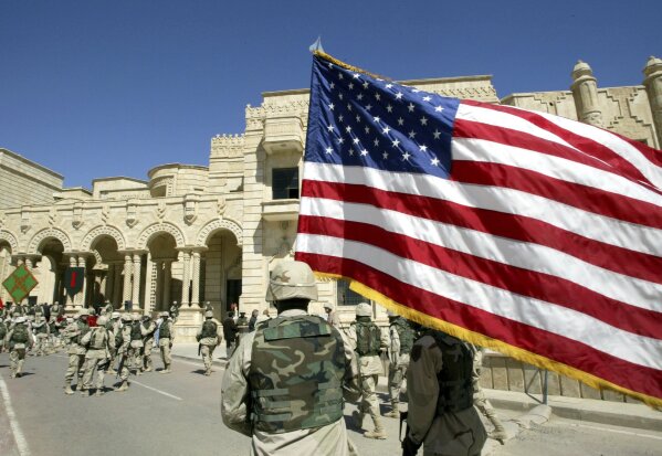 FILE - In this March 16, 2004, file photo, a U.S. soldier from the 1st Infantry Division walks with a U.S. flag after the changeover ceremony in one of ousted Iraqi President Saddam Hussein's palaces, now a U.S. army base, in Tikrit, about 110 miles (180 kilometers) northwest of Baghdad, Iraq. In Iraq, a country that still struggles with the controversial legacy of a U.S.-led invasion in the name of democracy, many people followed the Washington events with a mixture of shock and fascination. (AP Photo /Murad Sezer, File)
