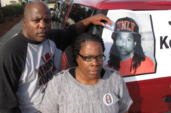 FILE - Kenneth and Jacquelyn Johnson stand next to a banner on their SUV showing their late son, Kendrick Johnson, on Dec. 13, 2013, in Valdosta, Ga. A Georgia sheriff who last year reopened an investigation into the 2013 death of Kendrick Johnson, a teenager found inside a rolled up gym mat at school, concluded, Wednesday, Jan. 26, 2022, there was no evidence of foul play after reviewing voluminous evidence collected by federal investigators. (AP Photo/Russ Bynum, File)