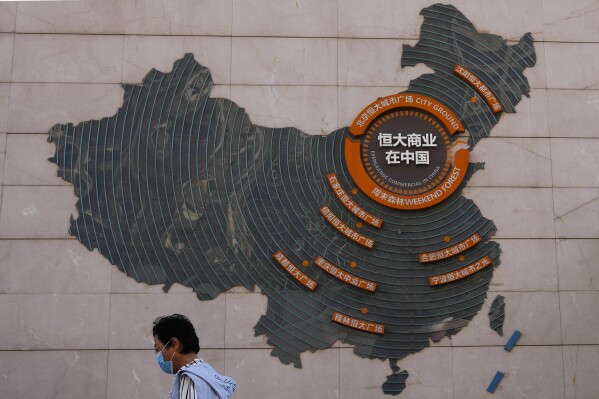 FILE - A woman walks past a map showing Evergrande development projects in China, at an Evergrande city plaza in Beijing on Sept. 21, 2021. Police in a southern Chinese city said on Saturday, Sept 17, 2023 they have detained some staff at China Evergrande Group's wealth management unit in the latest trouble for the heavily indebted developer. (AP Photo/Andy Wong, File)
