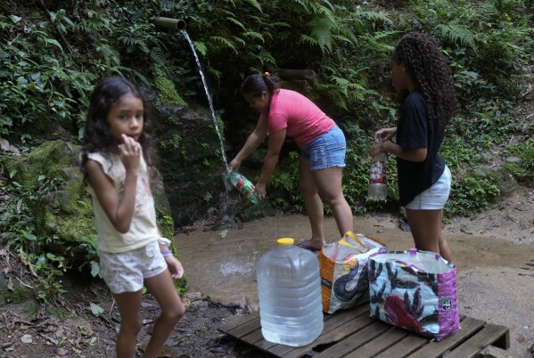 Residents collect drinking water that falls naturally down a mountain in the Rocinha favela of Rio de Janeiro, Brazil, Monday, March 18, 2024. (AP Photo/Silvia Izquierdo)