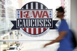 File-In this Feb. 4, 2020, file photo, a pedestrian walks past a sign for the Iowa Caucuses on a downtown skywalk, in Des Moines, Iowa. The Iowa Democratic Party is agreeing to recount the results in about two dozen of almost 1,700 precinct caucuses as part of the ongoing process to resolve the weeks-long question of who won Iowa's tarnished presidential caucuses. Campaign officials for former South Bend Mayor Pete Buttigieg and Vermont Sen. Bernie Sanders asked for a combined 23 precincts to be recounted. (AP Photo/Charlie Neibergall, File)